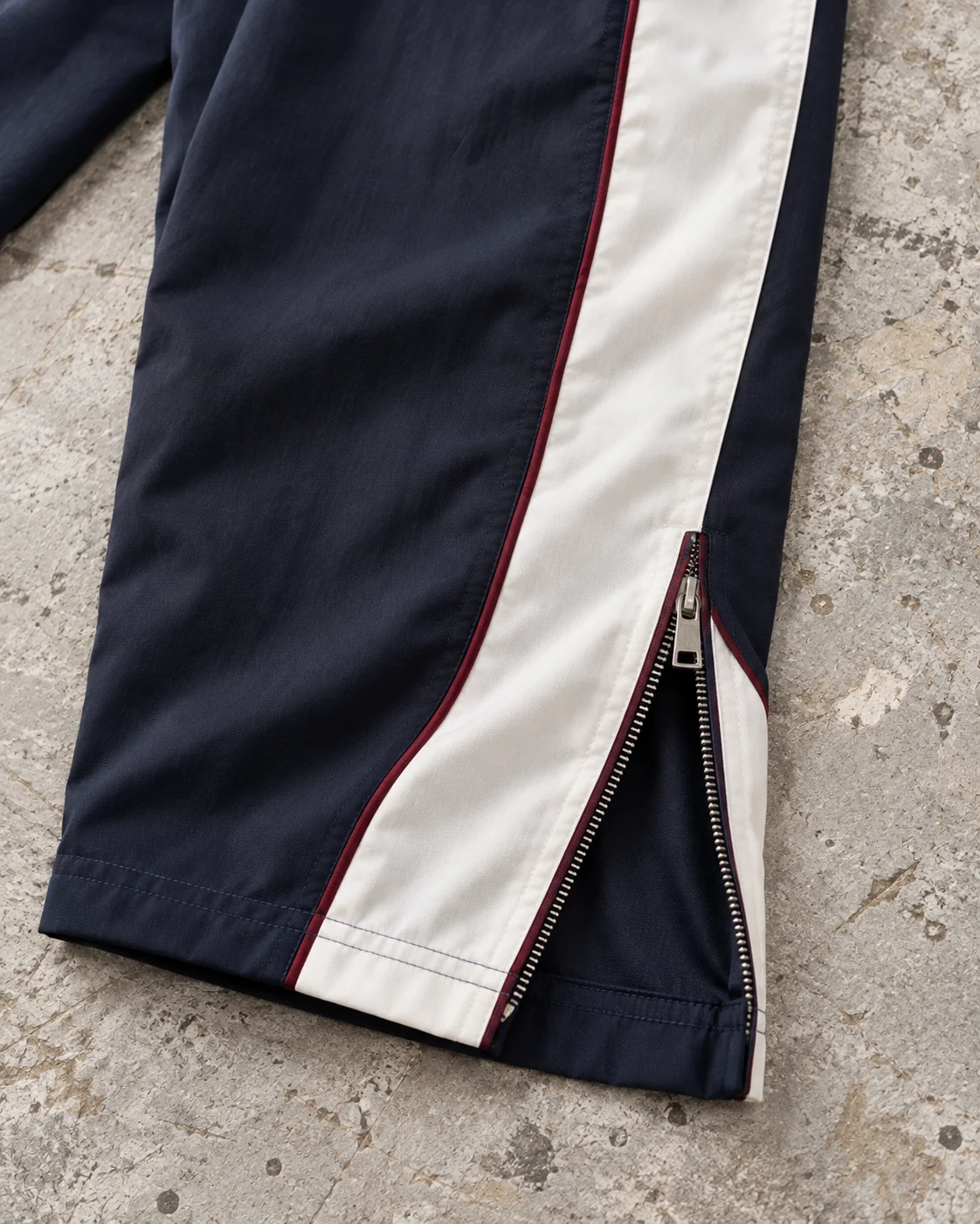 Close-up of fabric and signature construction — Panelled Track Pants in midnight navy / ivory / burgundy, AI-generated design concept